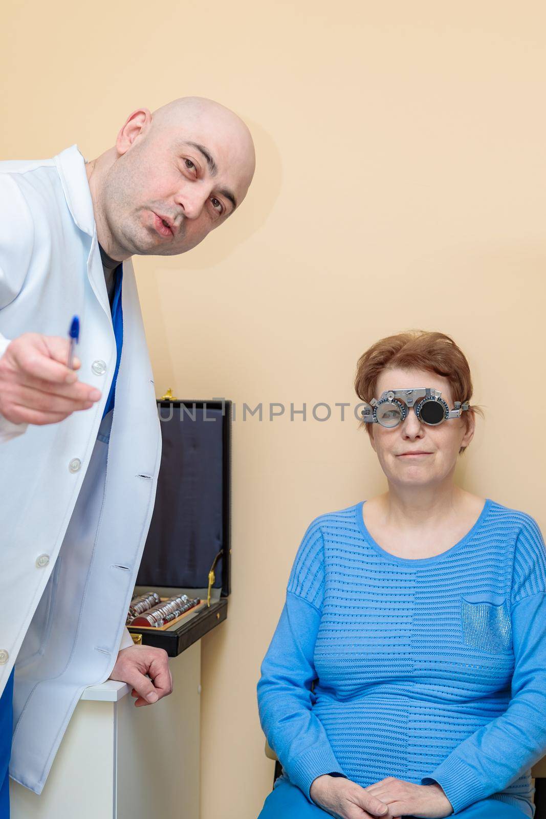 A male optometrist checks the eyesight of an adult woman with a trial frame.