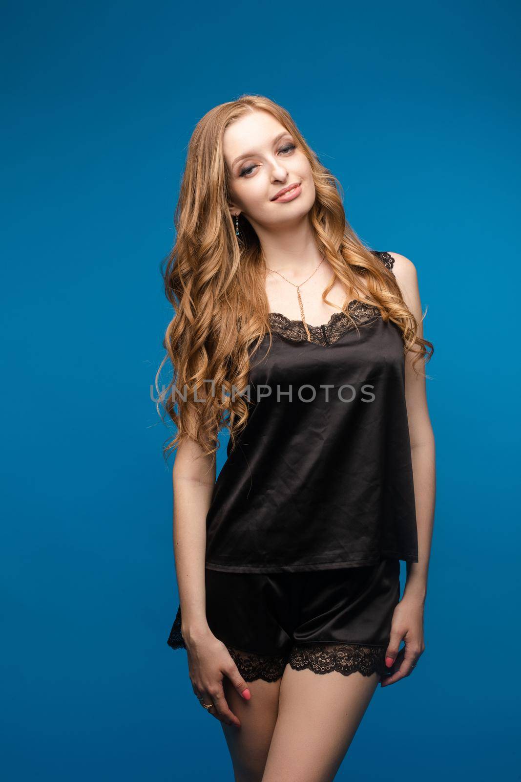 A woman with long beautiful hair in a black outfit on a blue background in the studio. by StudioLucky