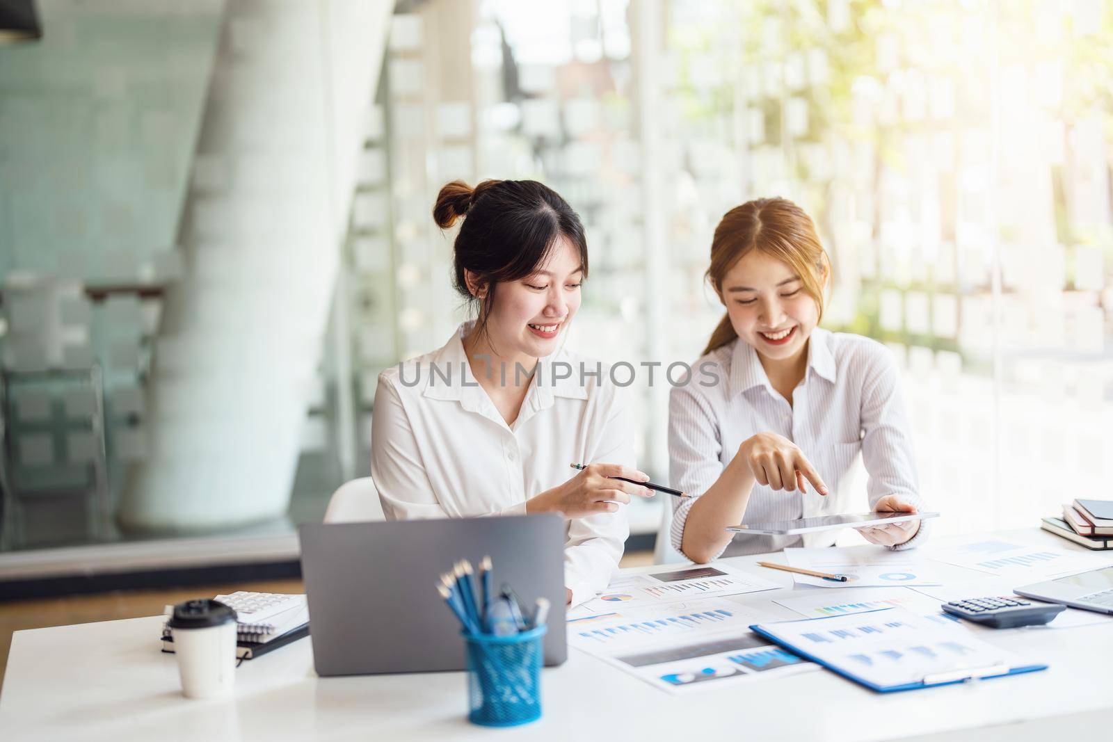 Negotiation, Analysis, Discussion: Portrait of an Asian female economist and marketer using tablet computer to plan investments and financial to prevent risks and losses for the company by Manastrong