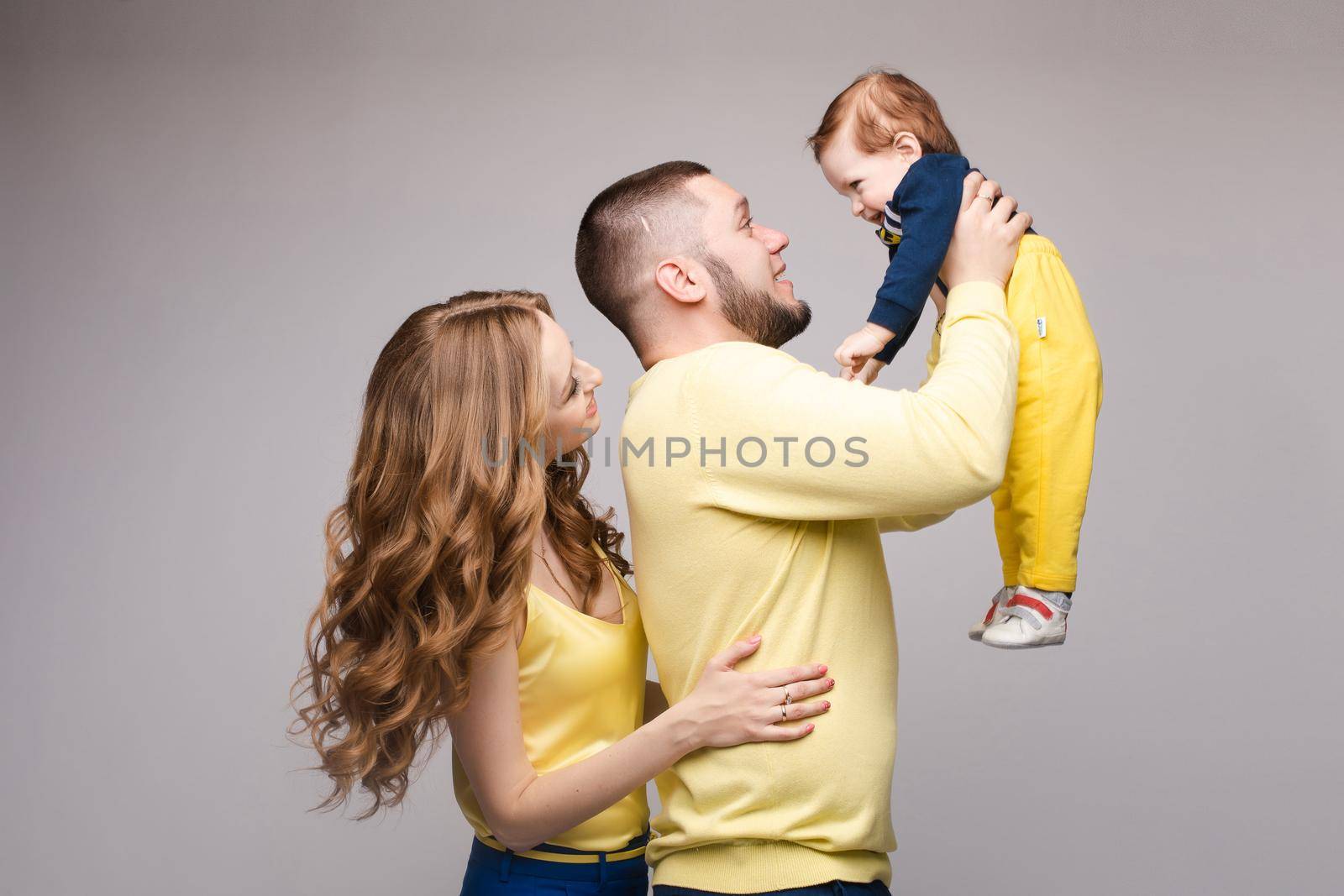 A beautiful family with a small child in the studio on a gray background. by StudioLucky