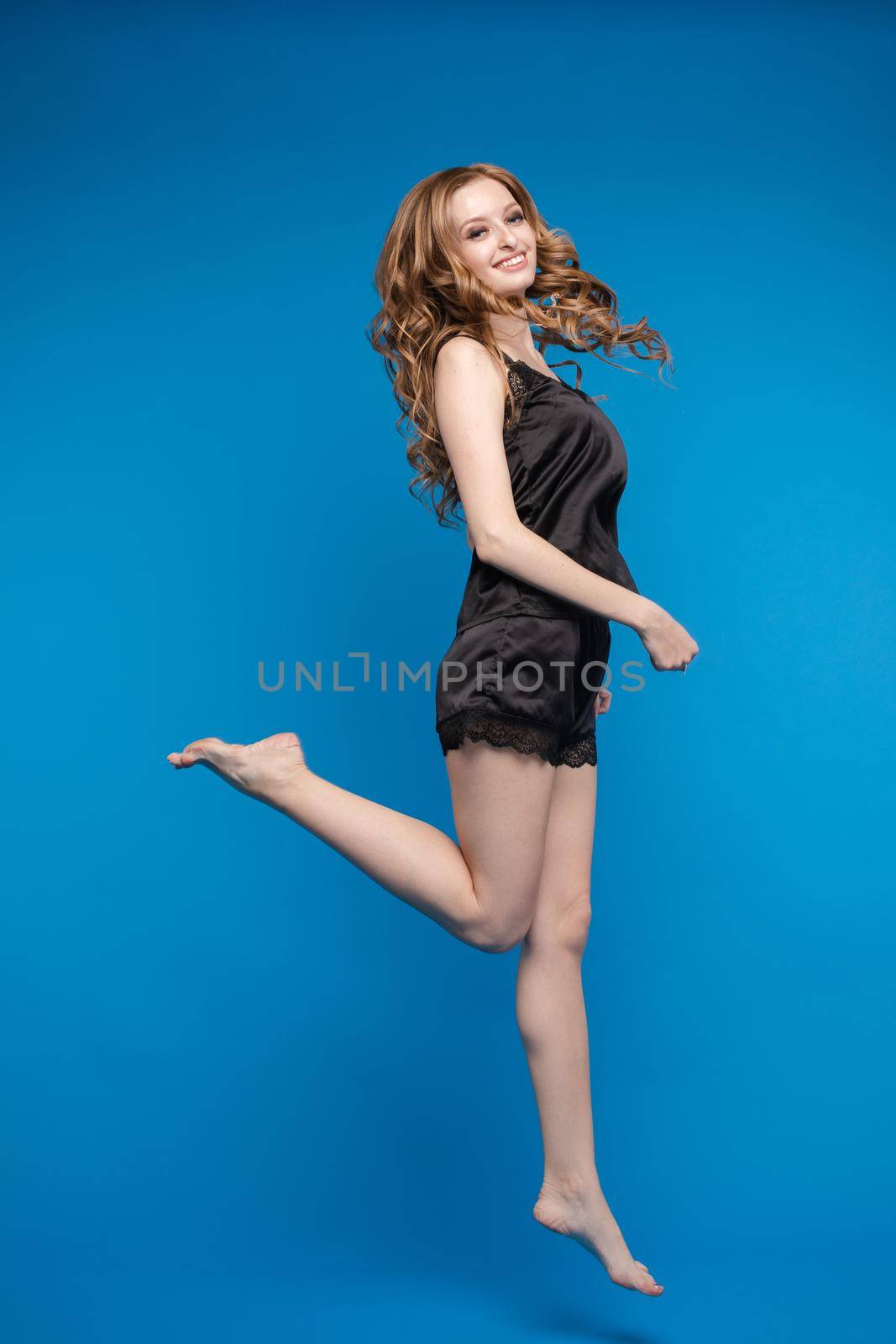 A woman with long beautiful hair in a black outfit on a blue background in the studio. by StudioLucky