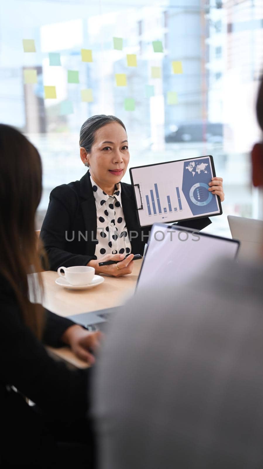 Senior female team leader holding digital tablet and giving presenting new marketing strategy at board room.