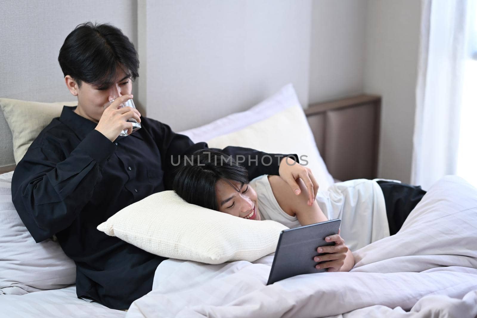 Loving homosexual couple embracing using digital tablet on bed. LGBT and love concept by prathanchorruangsak