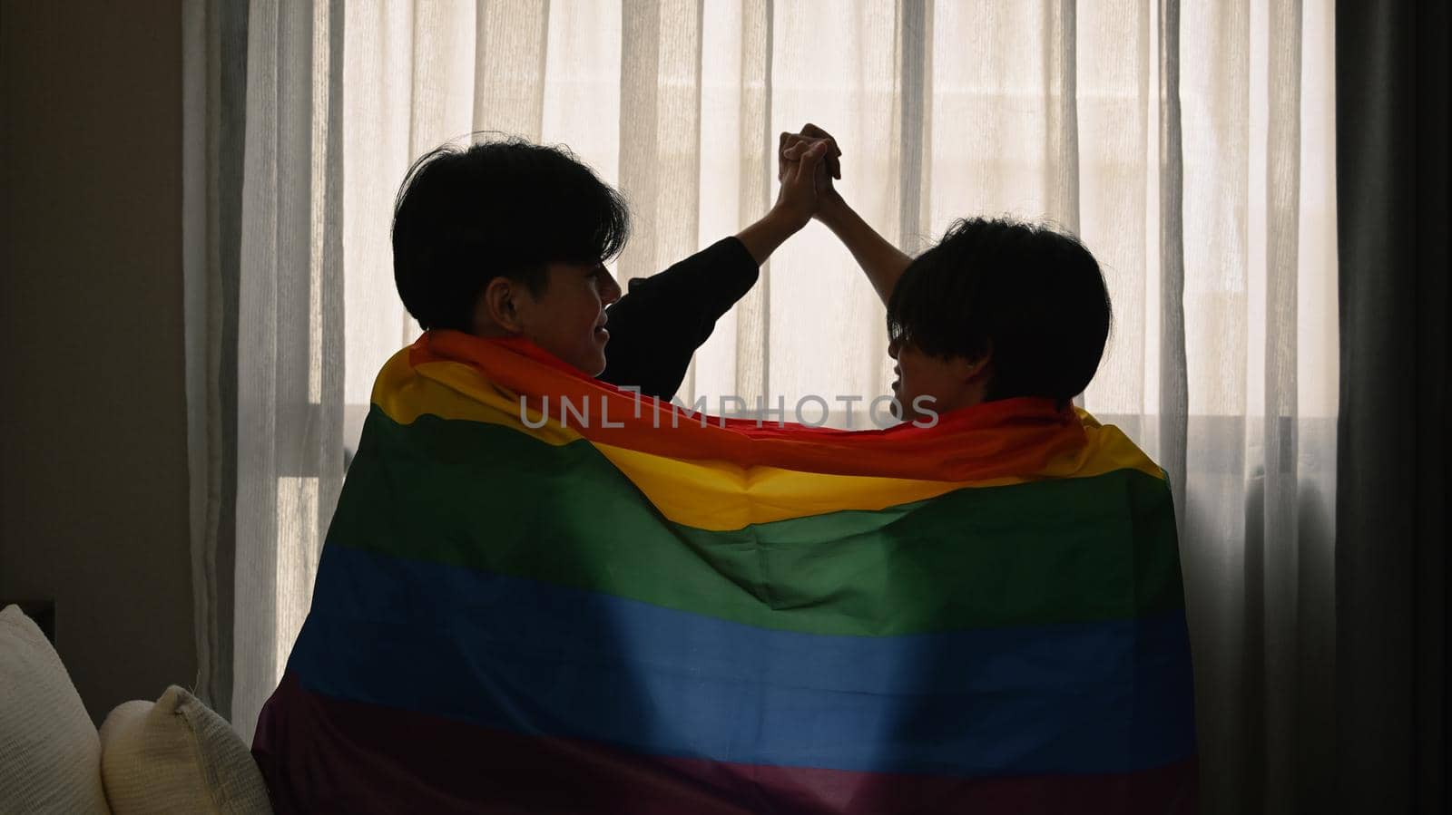 Happy gay couple expressing their love to each other under LGBTQ pride flag. Concept of sexual freedom and equal rights for LGBT community.