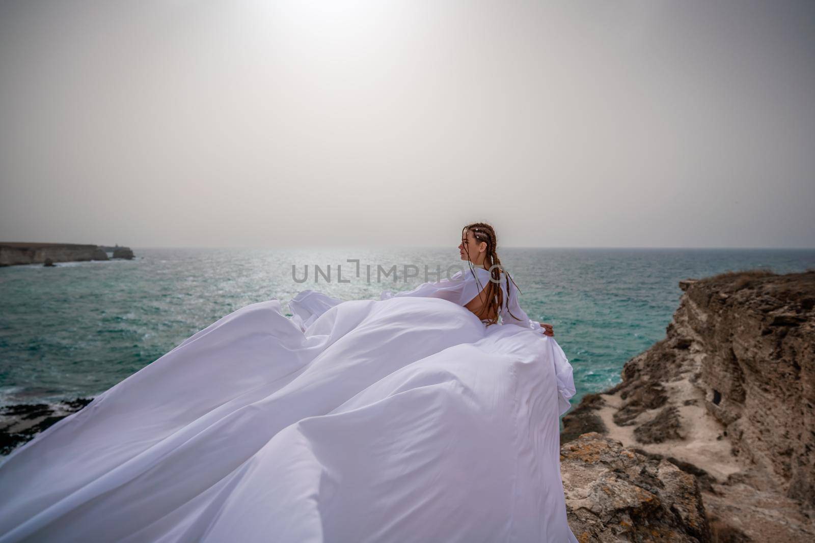 Happy freedom woman on the beach enjoying and posing in white dress. Rear view of a girl in a fluttering white dress in the wind. Holidays, holidays at sea