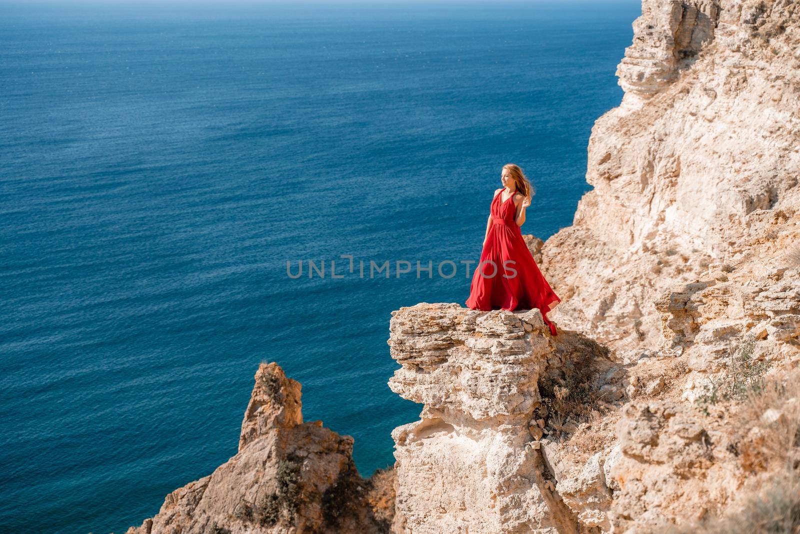 A woman in a red flying dress fluttering in the wind, against the backdrop of the sea