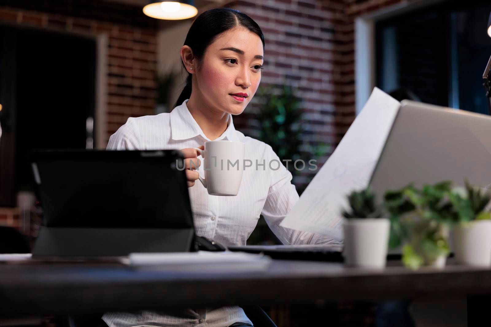 Confident marketing company accountant with modern tablet reviewing startup project documentation paperwork. Executive manager with electronic touchscreen handheld device sitting in office workspace.