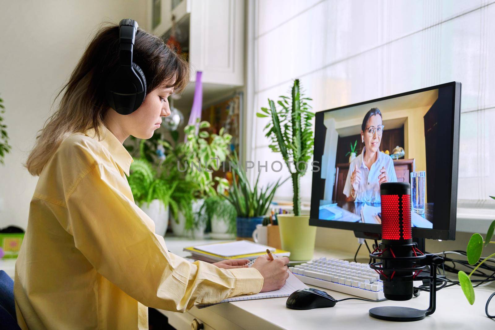 Teenage female student studying online at home, female in headphones with notebook talking to teacher by video, using computer. Chat call conference, e-learning college high school, technology concept