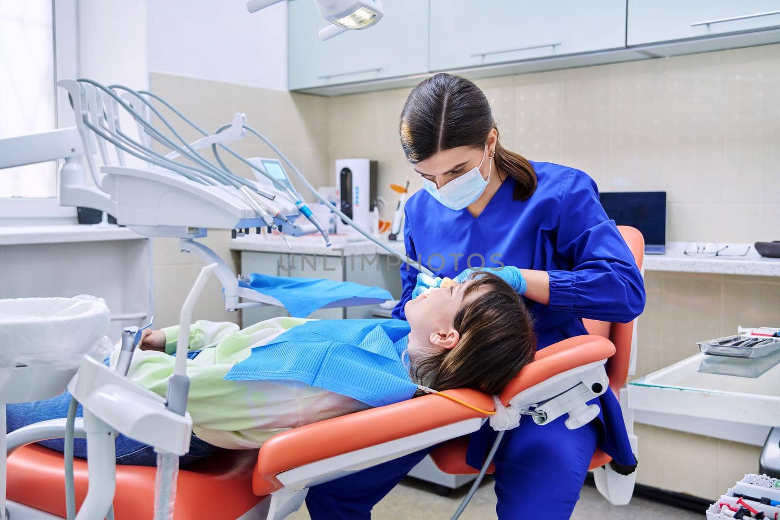 Doctor dentist treats teeth to a young teenage female patient. Real process of treatment, dental care, orthodontics, therapy, health care, dentistry concept