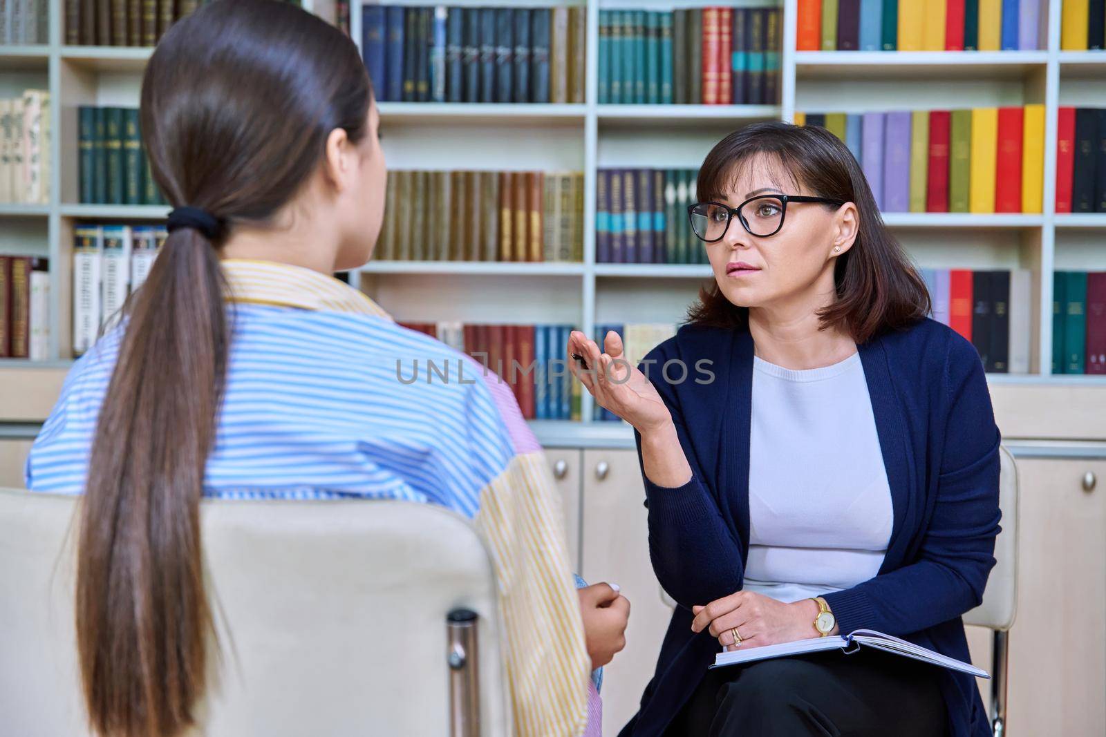 Female teacher, psychologist talking to female student in library. School counselor in individual session with teenage girl in office. Psychologists, therapy, high school, college, adolescence concept