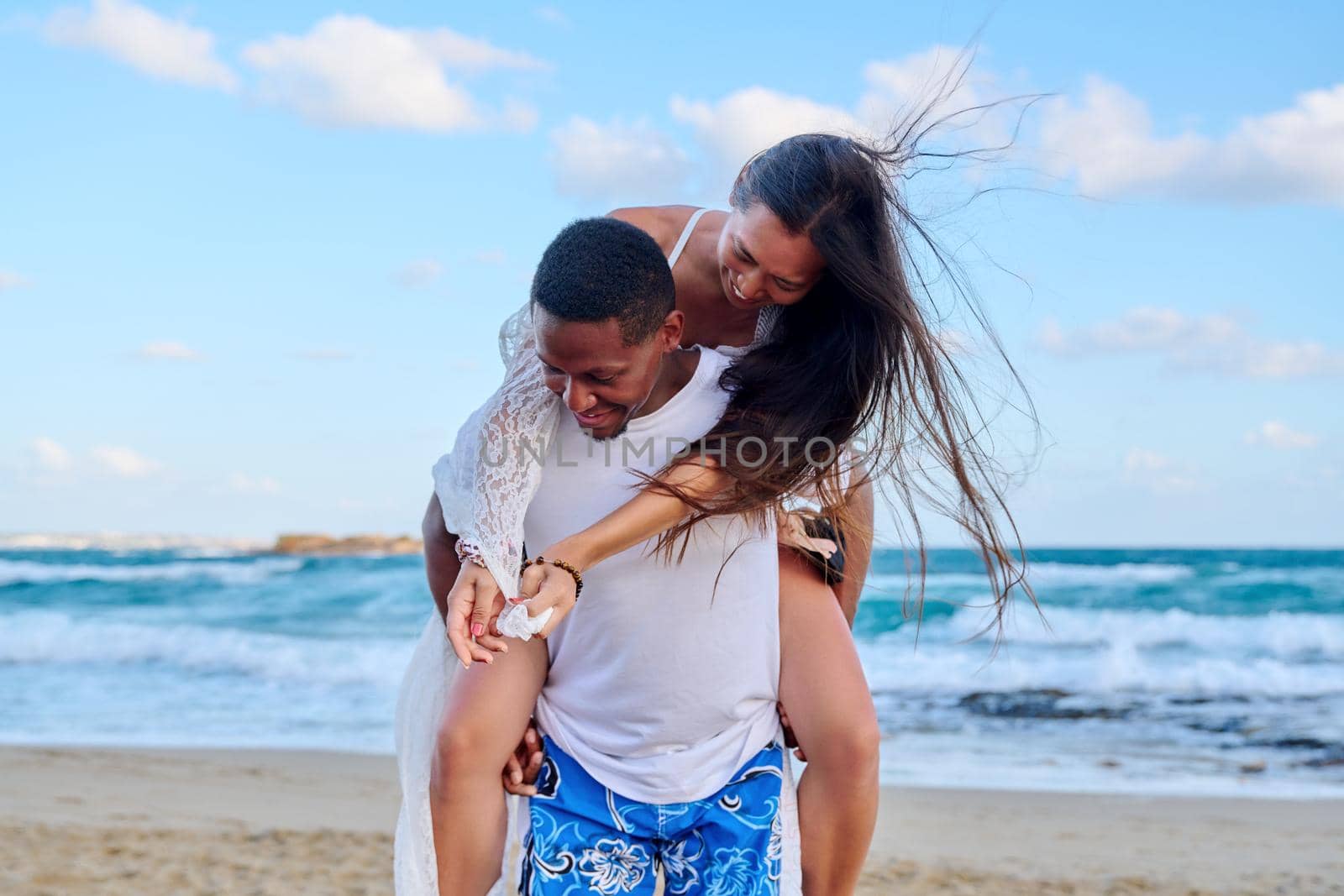 Happy young beautiful couple having fun on beach. Afro american asian couple laughing enjoying vacation in seaside nature. Multicultural, multiethnic family, relationships, togetherness, lifestyle