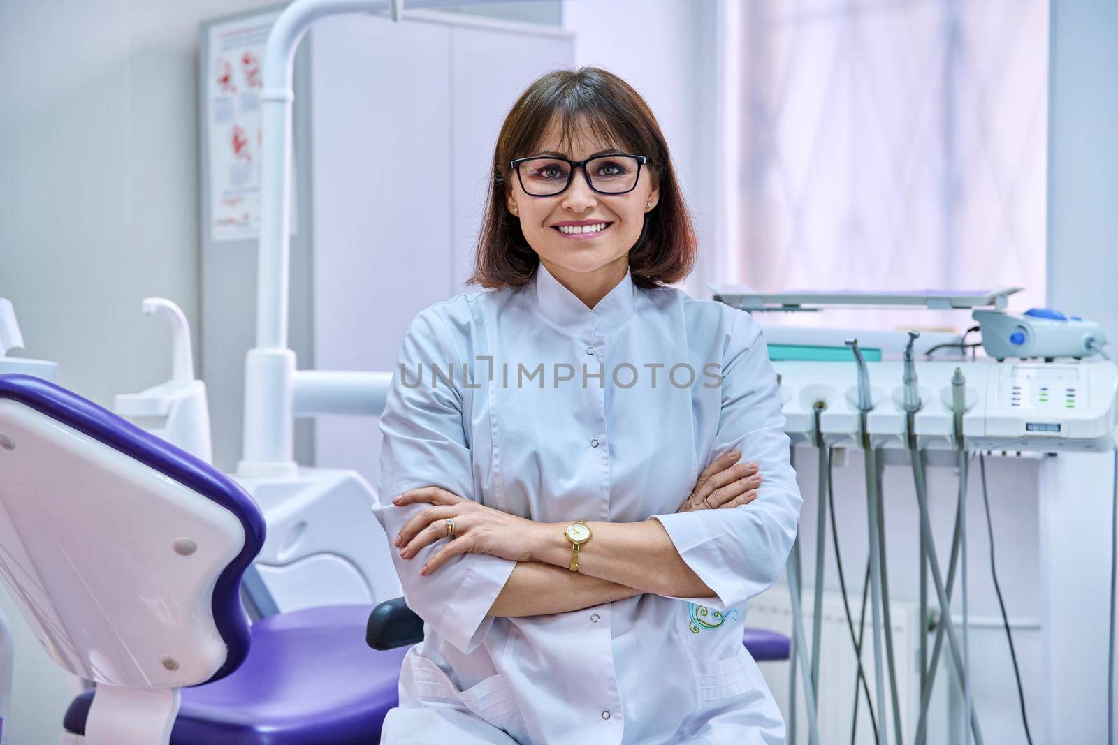 Portrait of confident female dentist in office looking at camera. Middle aged female doctor with crossed arms. Dentistry, medicine, health care, profession, stomatology concept
