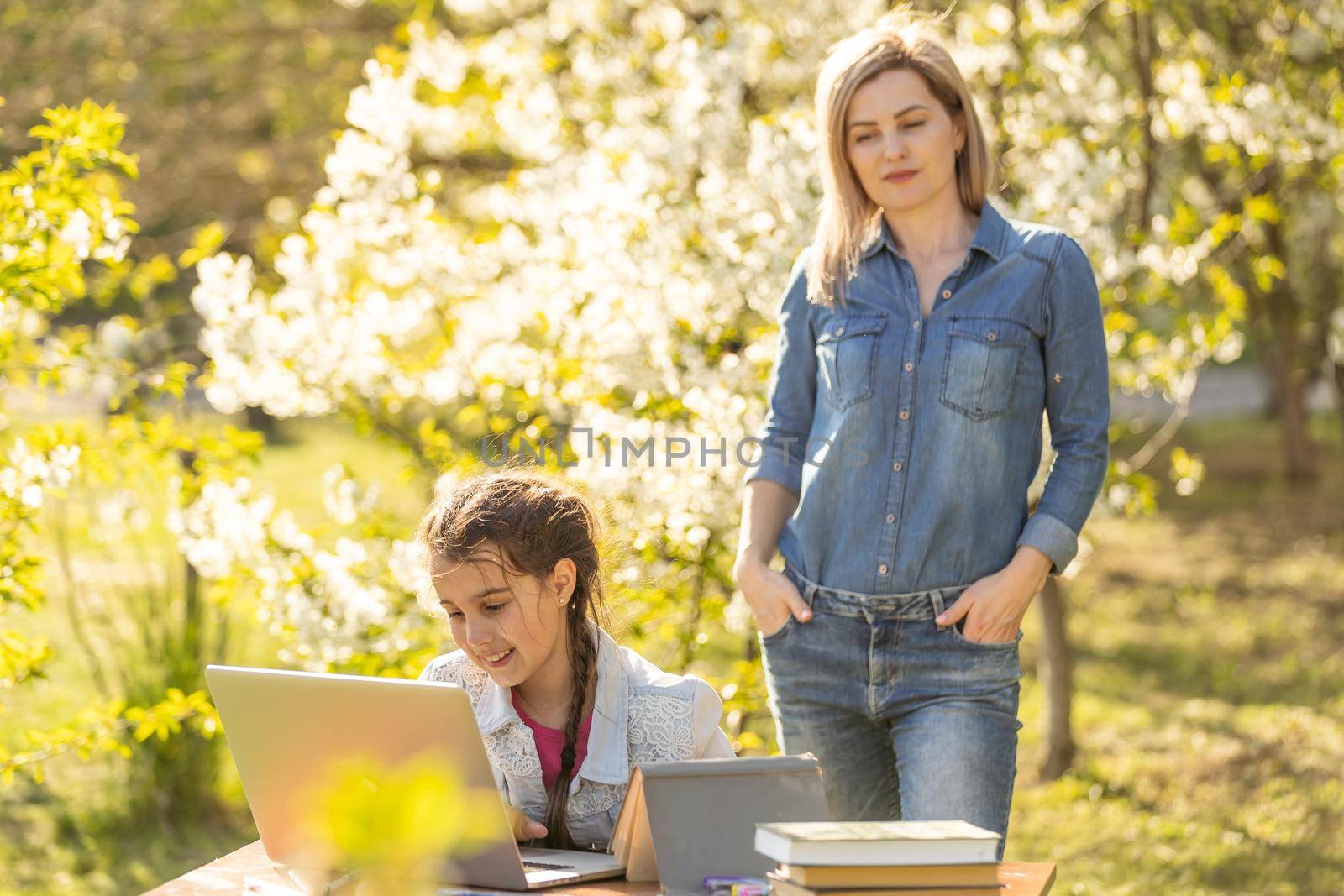 Mother helping her little daughter to use laptop computer. Child studying at home doing her homework or having online lesson. Homeschooling concept