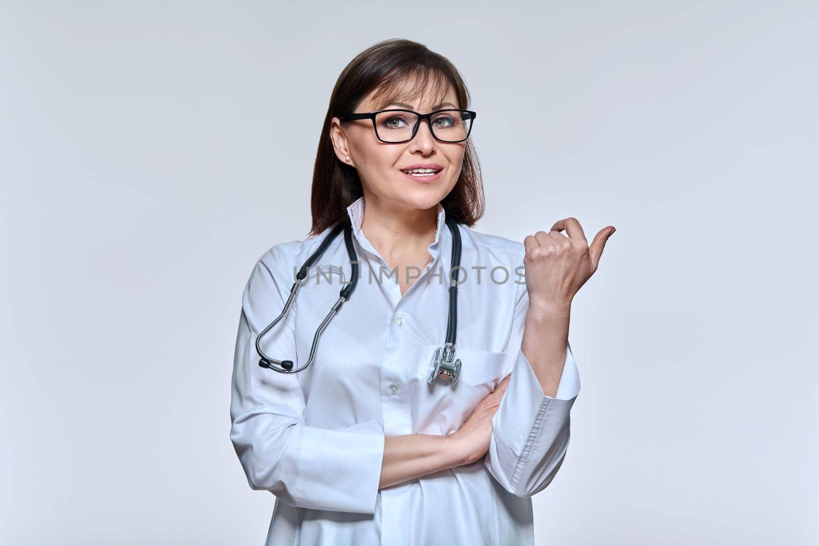 Portrait of female doctor looking at camera talking gesturing on light studio background. Confident doc in white uniform glasses with stethoscope. Consultation, conversation, medicine, health care