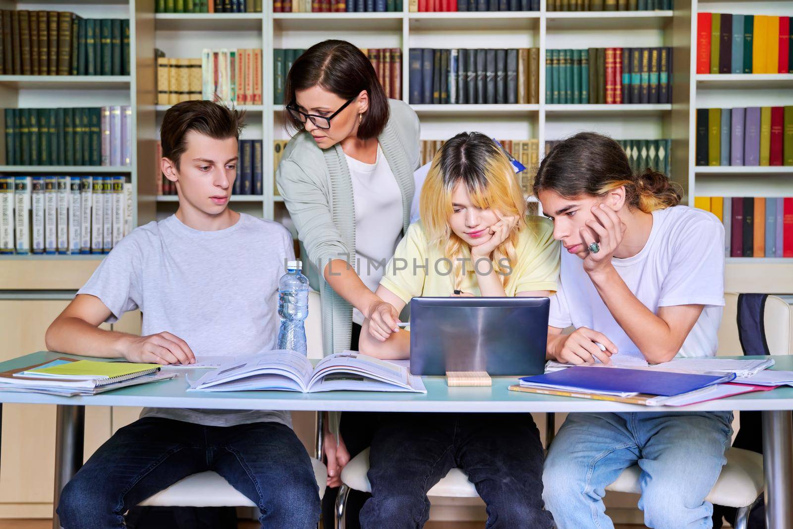 Group of teenage students studying in library class with female teacher mentor by VH-studio