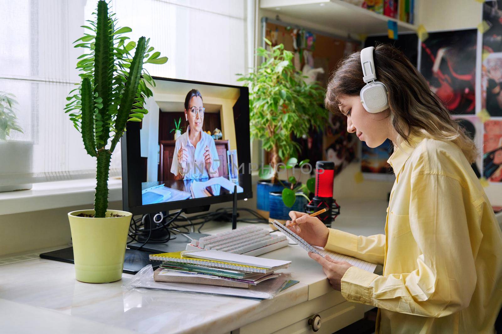 Teenage female student studying online at home, female in headphones with notebook talking to teacher by video, using computer. Chat call conference, e-learning college high school, technology concept