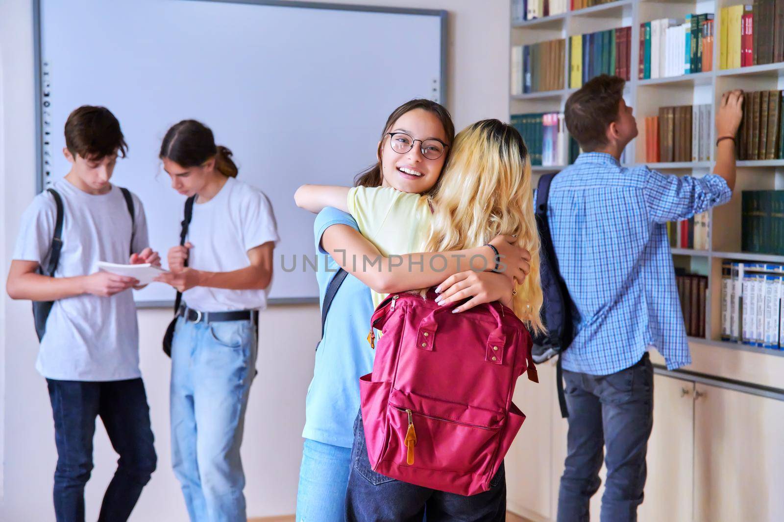 Students girls hugging at the meeting, a group of teenagers in the school library. Friendship communication, adolescence, high school, education concept