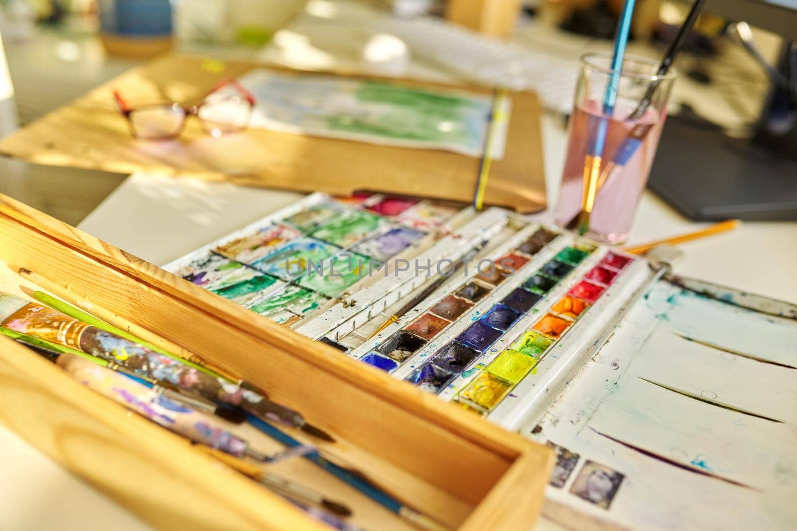 Drawing, artwork, hobby, education, creativity concept. Close-up of watercolor drawing, glasses, watercolor paints in box, brushes on the table, nobody