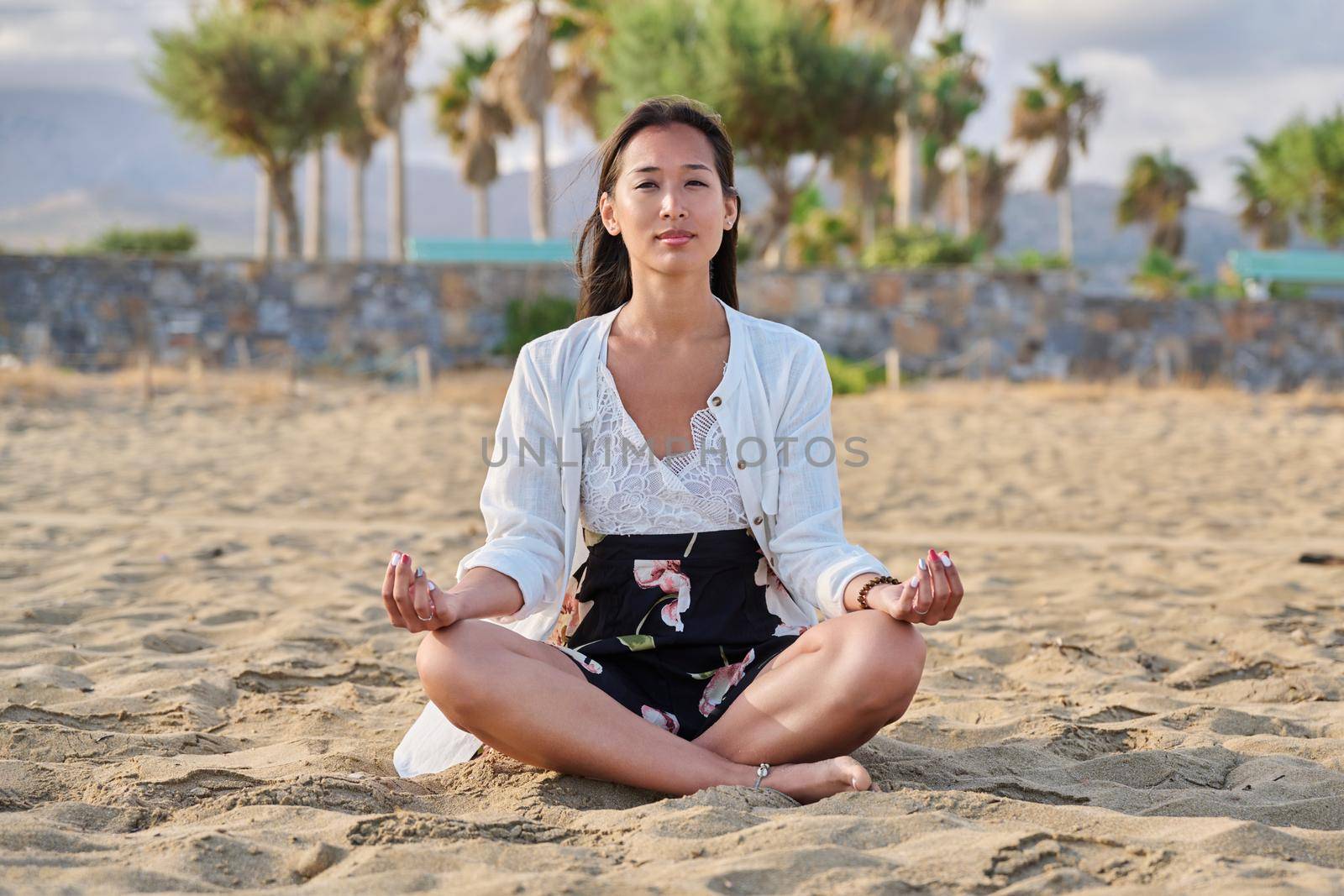 Young woman practicing yoga on beach. Beautiful Asian female meditating, sitting in lotus position on sand, on seashore. Beauty, lifestyle, meditation, relaxation, lifestyle, nature, people concept