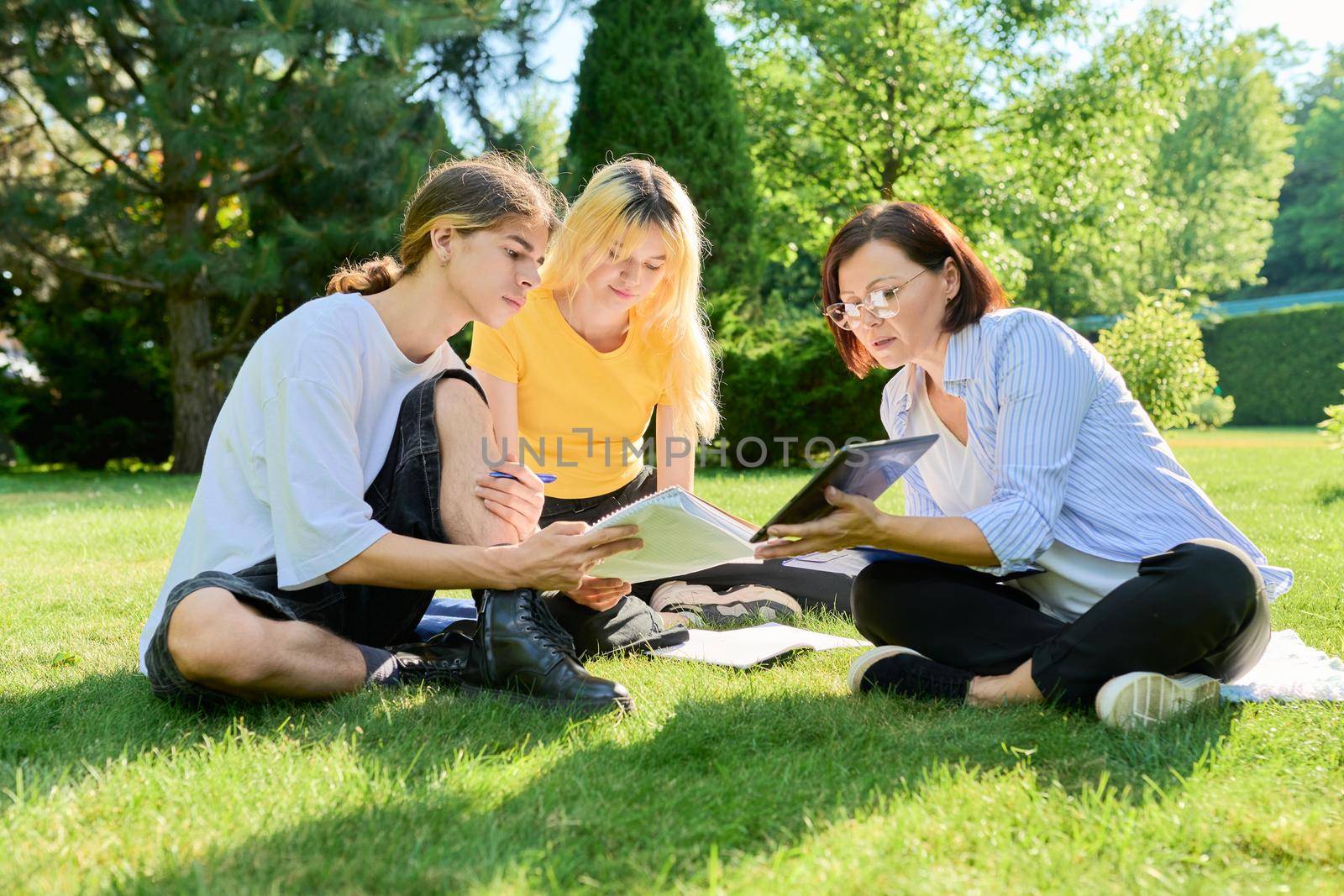 School teacher, psychologist, social worker talking to teenagers, sitting on grass by VH-studio