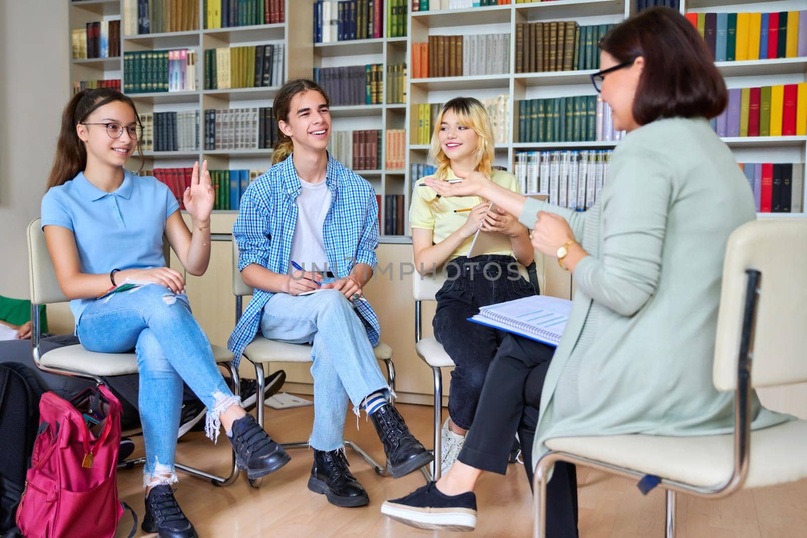 Group of teenage students with female teacher in library. High school students talking to mentor. Education, learning, knowledge, adolescence concept