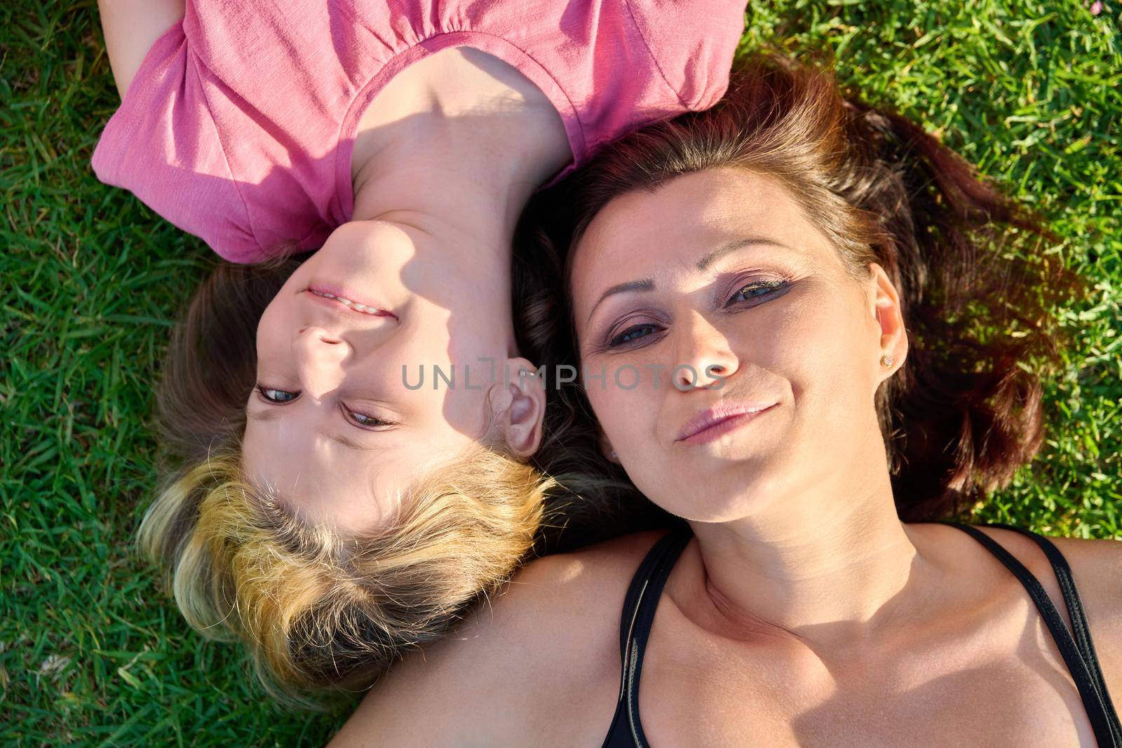 Happy mom daughter child lying on green grass, top view. Smiling faces of mother and girl 10, 11 years old. Family, mothers Day, motherhood, childhood, love, happiness concept