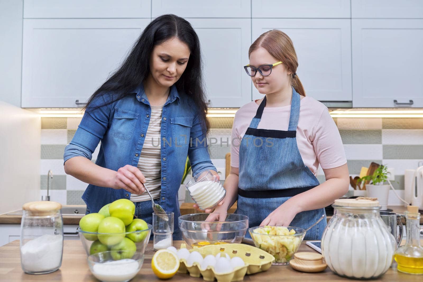 Mother and teenage daughter cooking at home in the kitchen. by VH-studio