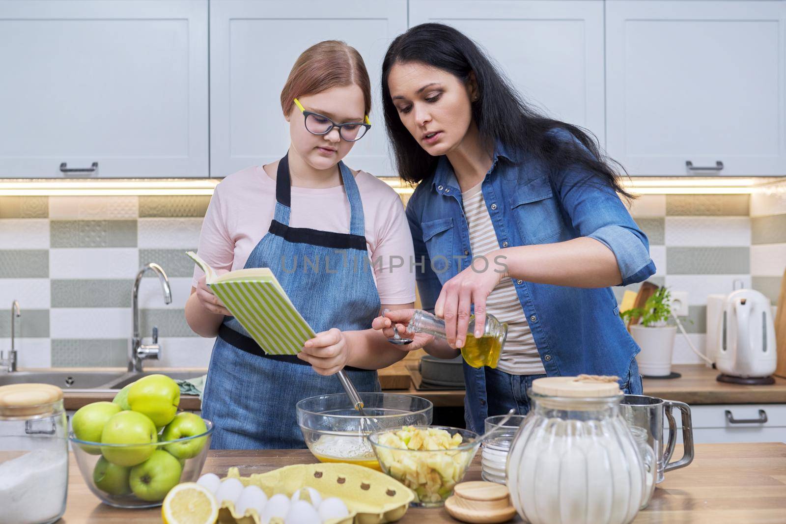 Mother and teenage daughter cooking at home in the kitchen. by VH-studio