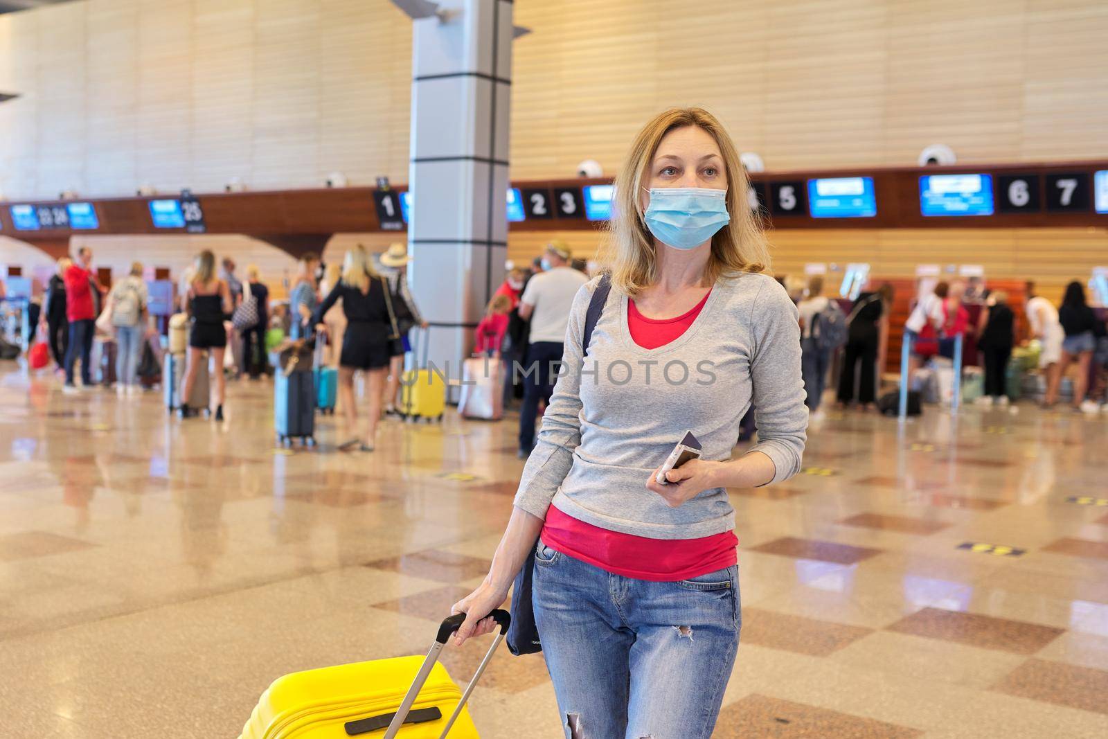 Woman passenger in medical protective mask at the airport with luggage suitcase. Tourism, travel, journey, transportation, vacation, trip concept
