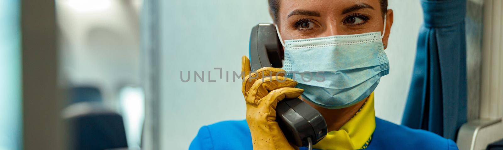 Close up of female flight attendant in protective face mask having phone conversation in aircraft cabin