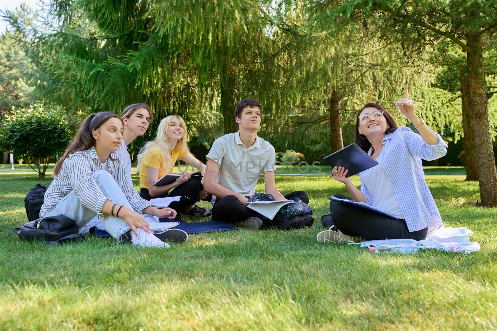 Outdoor, group of students with female teacher sitting on grass by VH-studio