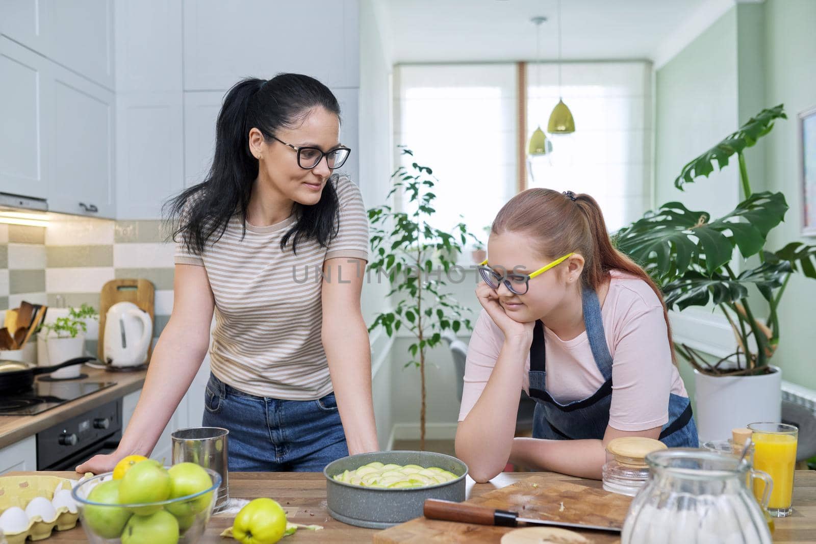Mother and teenage daughter cooking at home in kitchen. Mom and girl making apple pie together, talking smiling. Relationships, communication parent teenager, healthy homemade food, family concept