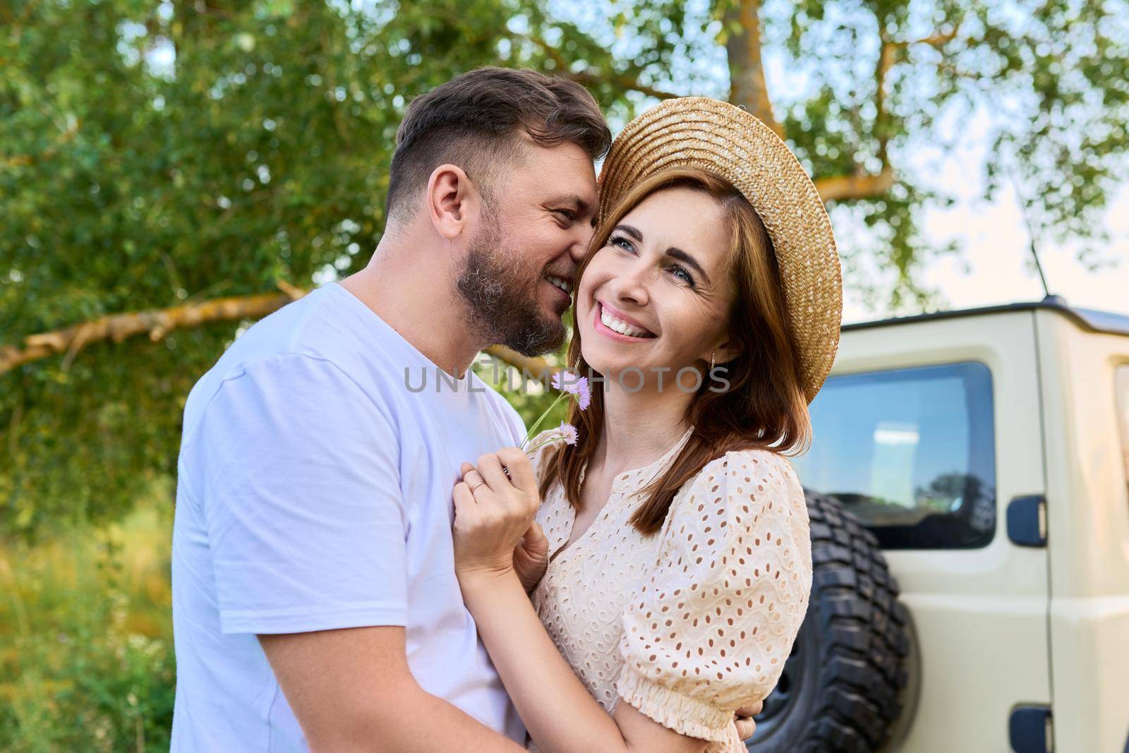 Love and romance of middle-aged couple. Happy hugging man and woman near car, summer nature wild meadow background. Relationship, holiday, date, trip, journey, weekend, family, people 40s concept