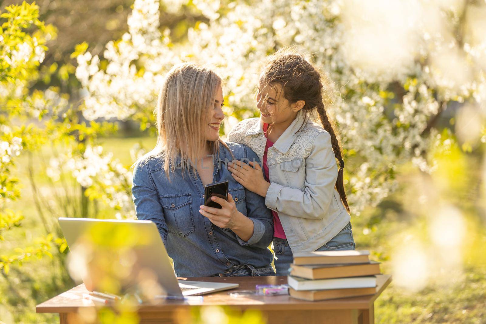 Mother daughter spending time outside. Mom and kid using laptop in nature.