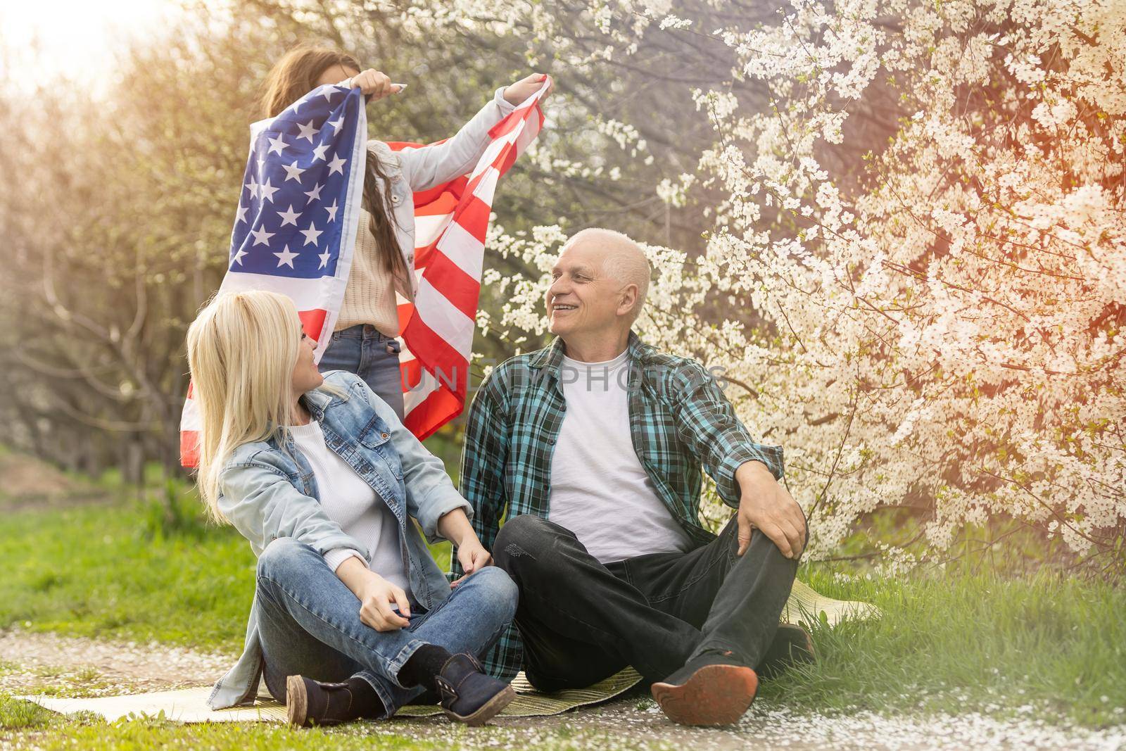 Portrait of happy family celebrating 4th July Independence Day holding silhouette usa national flag against park.