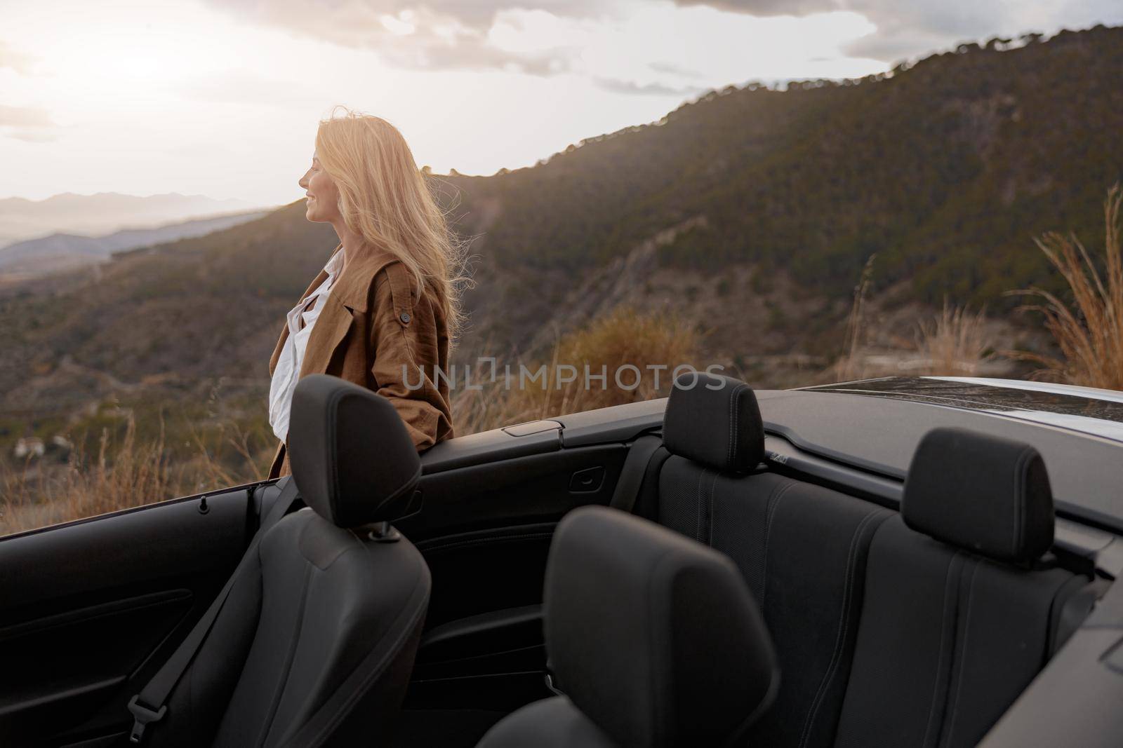 Side view of cheerful positive woman standing near convertible car looking away and smiling by Yaroslav_astakhov