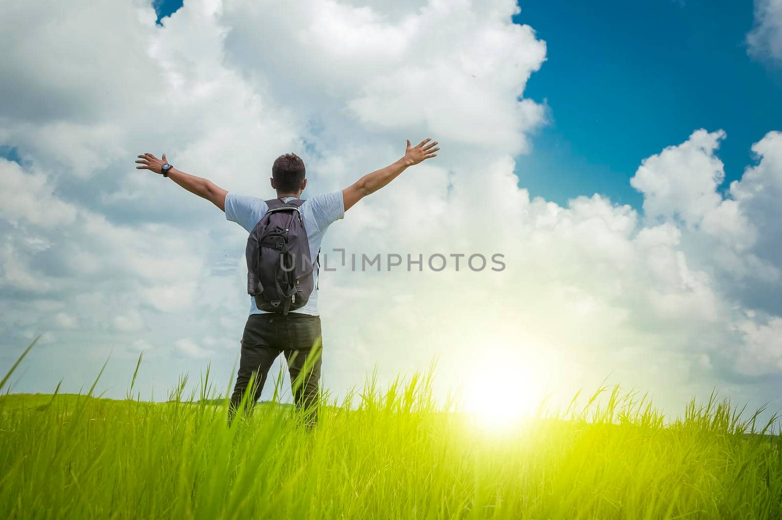 A backpacker on a hill with blue sky and copy space, man backpacking on a green hill with copy space, concept of successful man spreading his hands