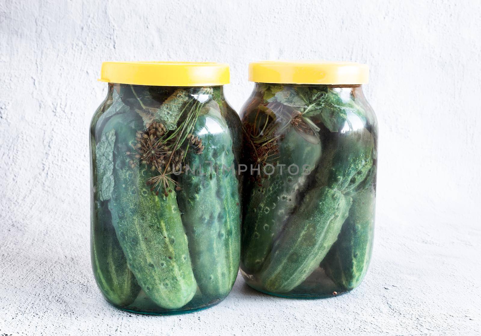 Two glass jars with pickled cucumbers, covered with lids. The concept of preserving organic products. Front view, copy space.