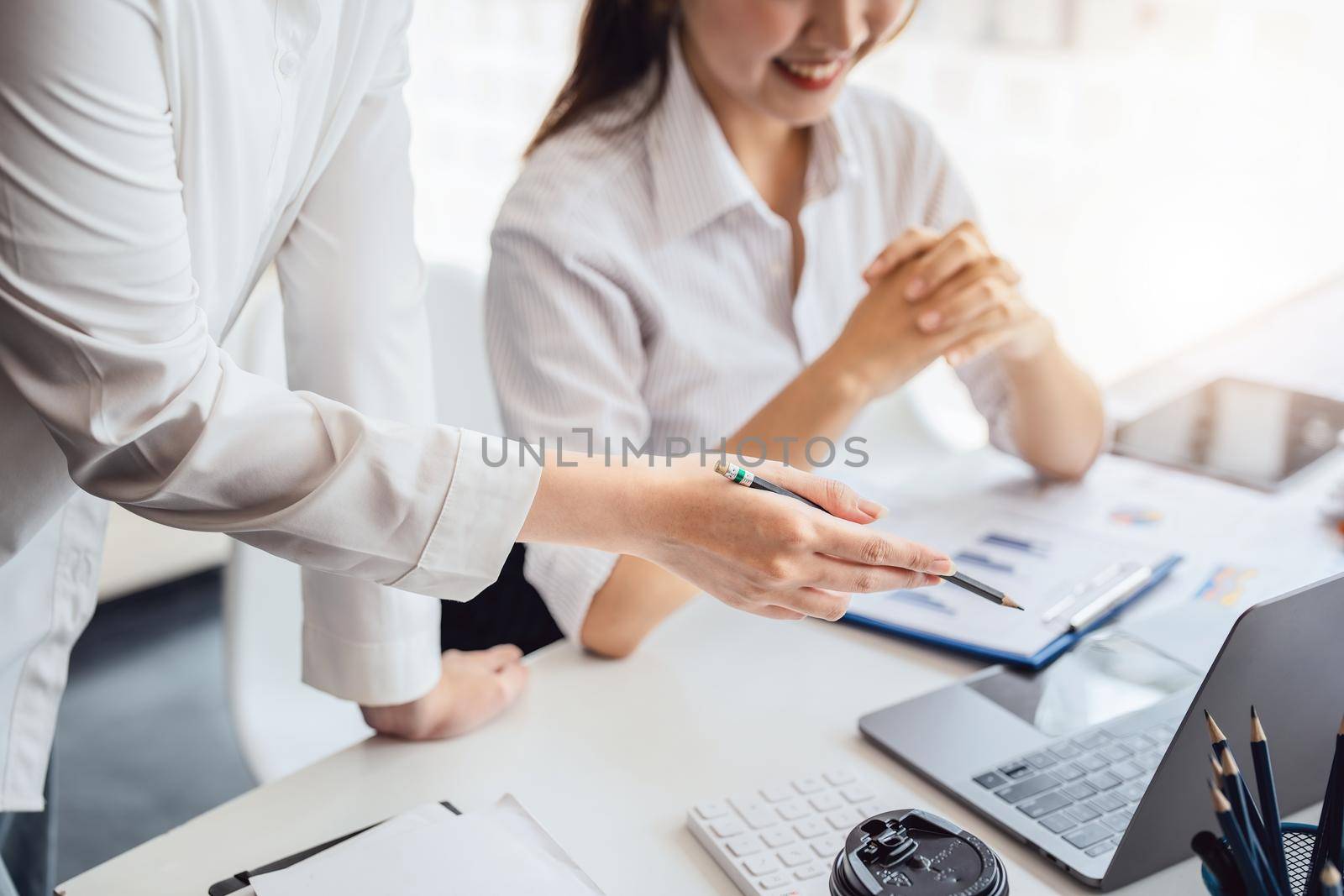 Negotiation, Analysis, Discussion: Asian female economist and marketer pointing to a financial data sheet to plan investments to prevent risks and losses for the company.