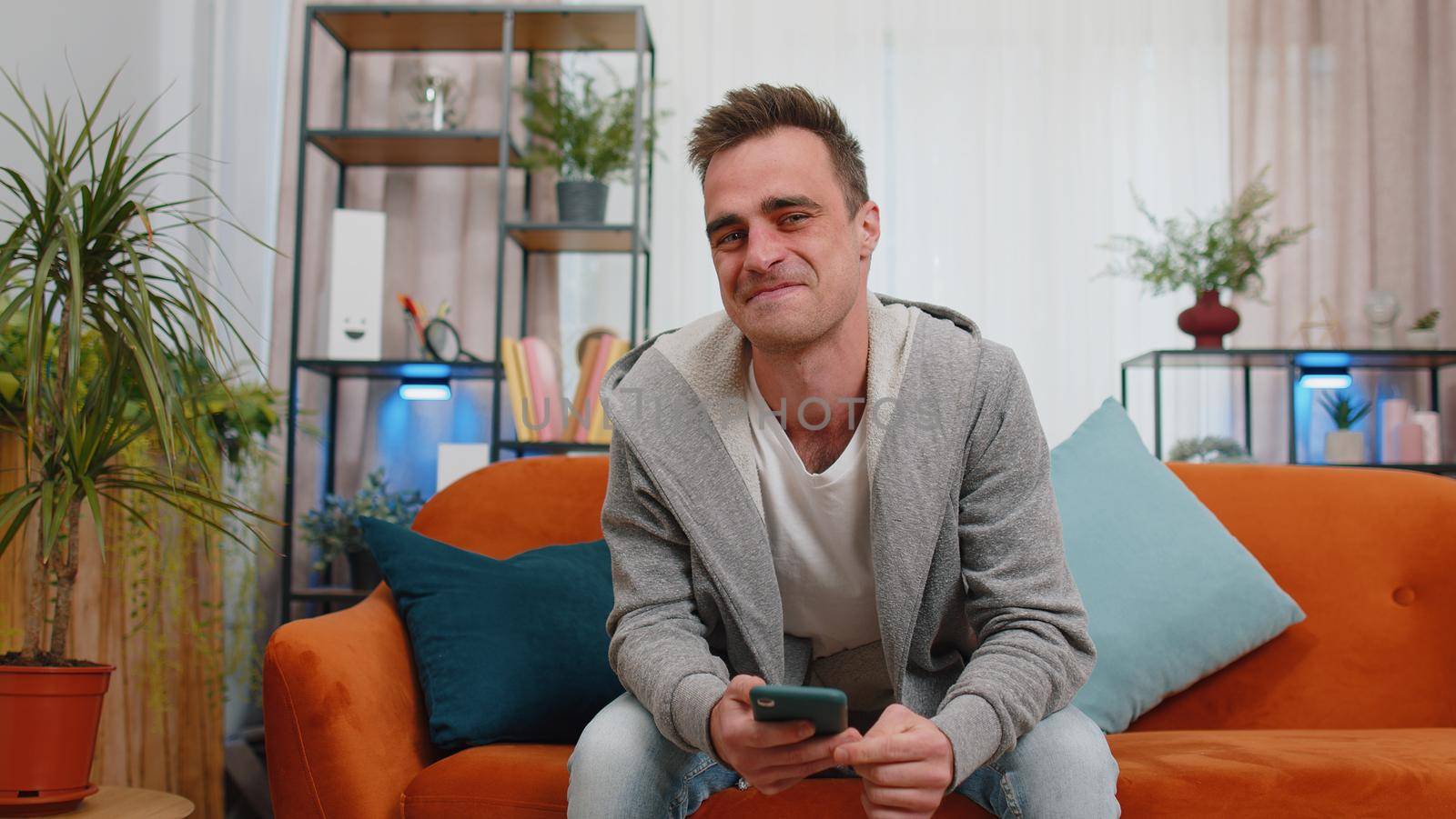 Excited happy caucasian man use mobile cell phone typing browsing say Wow yes found out great big win good news celebrate doing winner gesture. Young adult 20s guy at home in living room lying on sofa