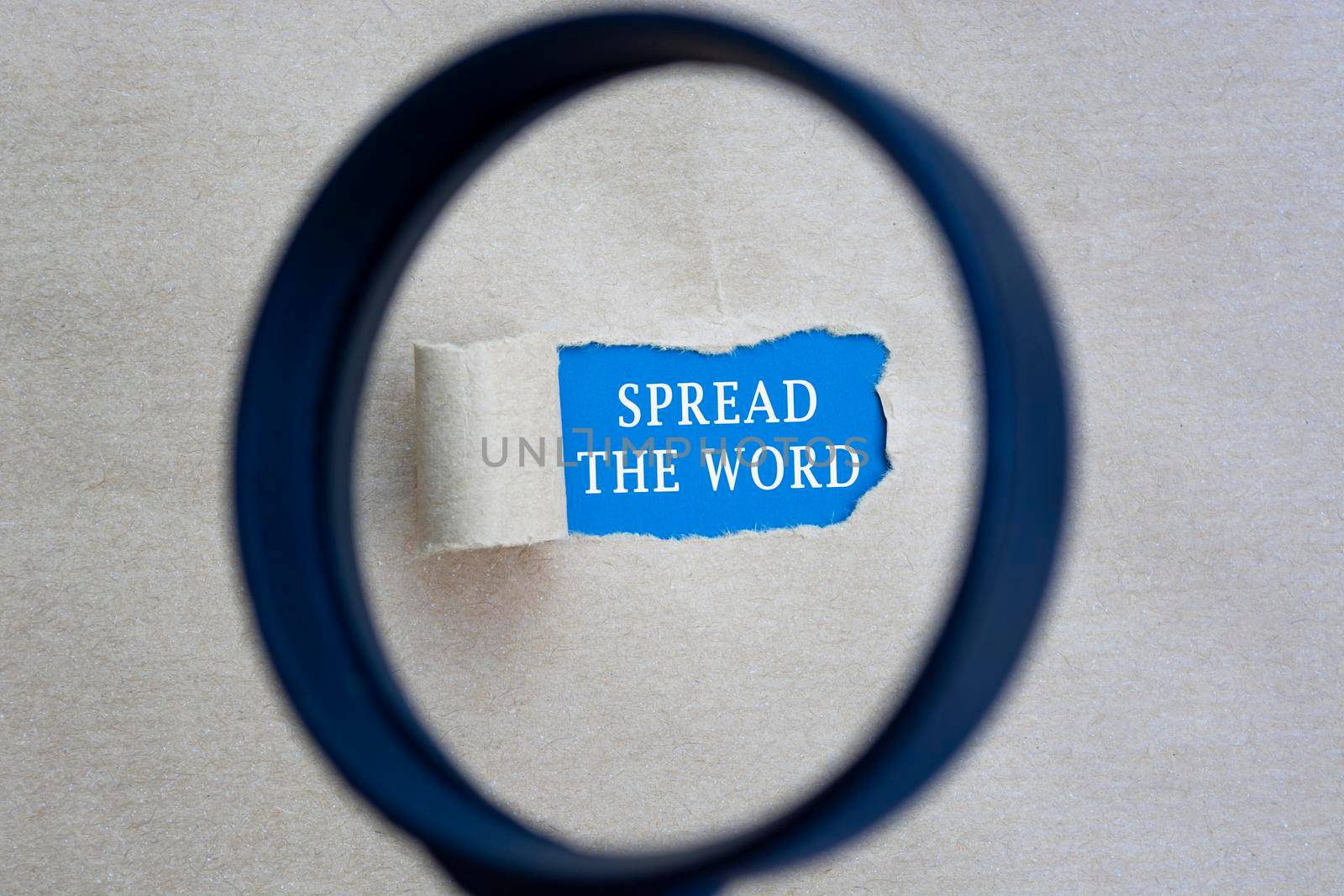 Spread the word text on torn hole in the sheet of brown paper on blue background with magnifying glass. Website, search and network concept.