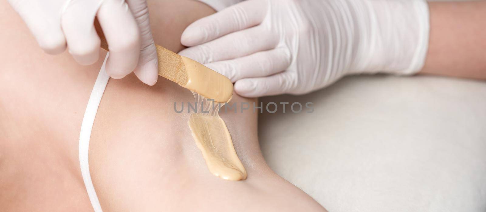 Depilation and epilation female armpit with liquid sugar paste by spatula. Hand of cosmetologist applying wax paste on armpit. Smooth underarm concept