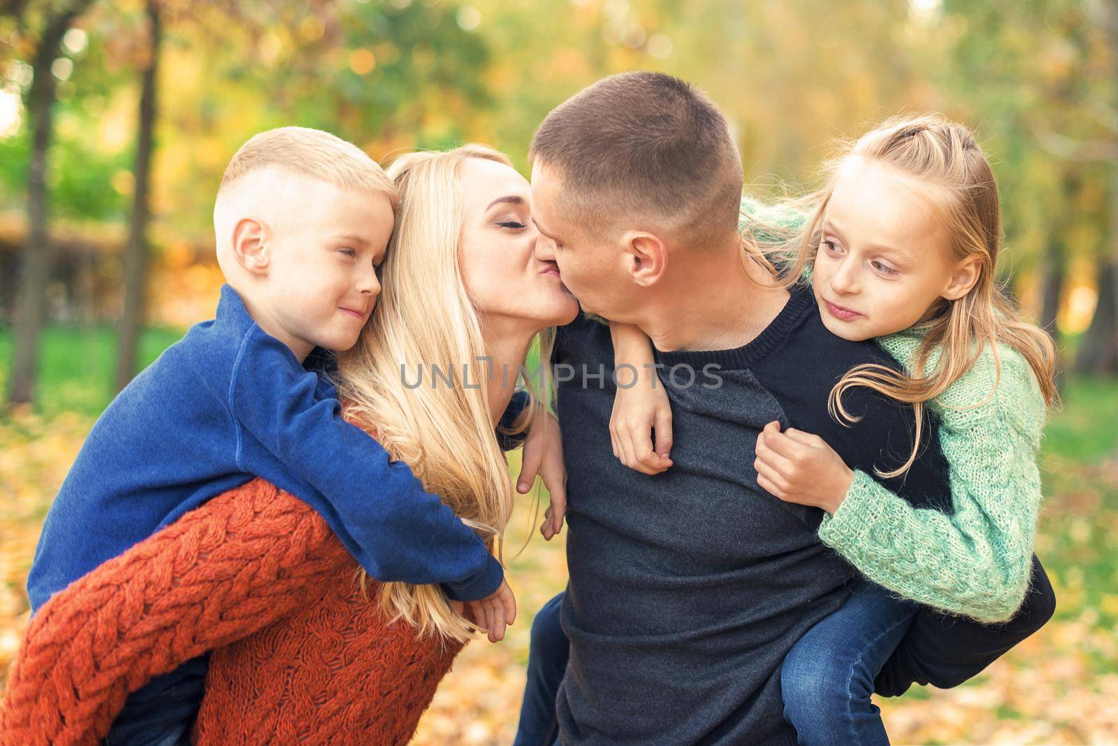Portrait of young family playing in autumn park. Parents kissing and resting with children in the autumn park