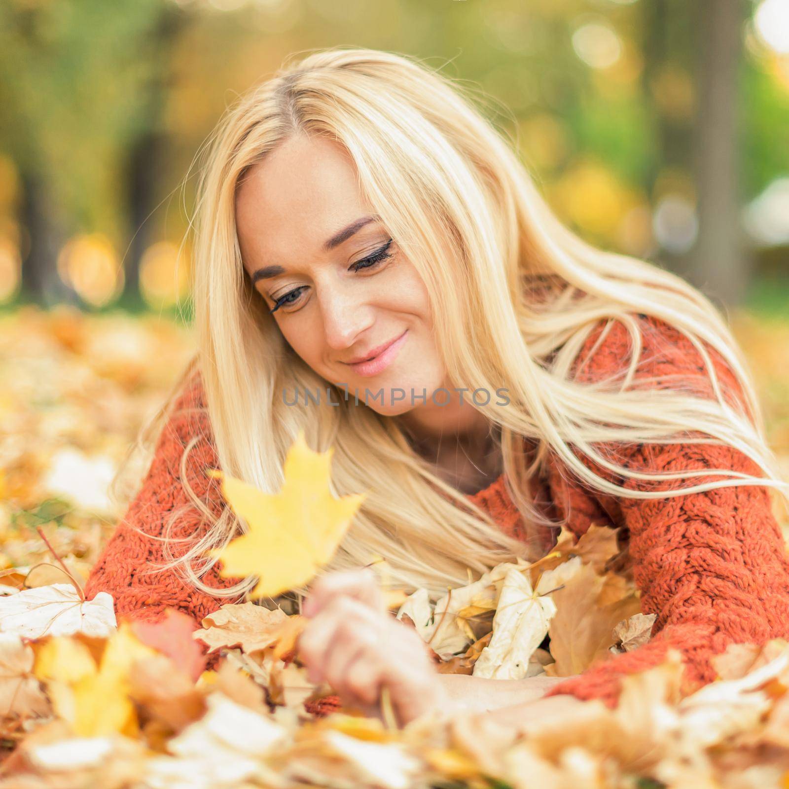 Beautiful young blond hair caucasian woman lies down on leaves at the autumn park