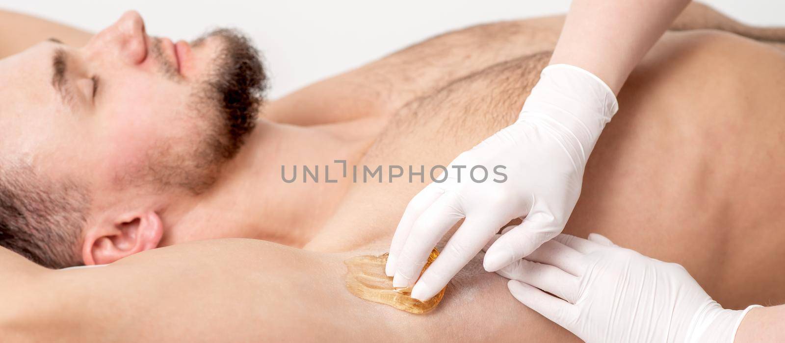 Depilation and epilation male armpit with liquid sugar paste. Hand of cosmetologist applying wax paste on armpit of man. Smooth underarm concept