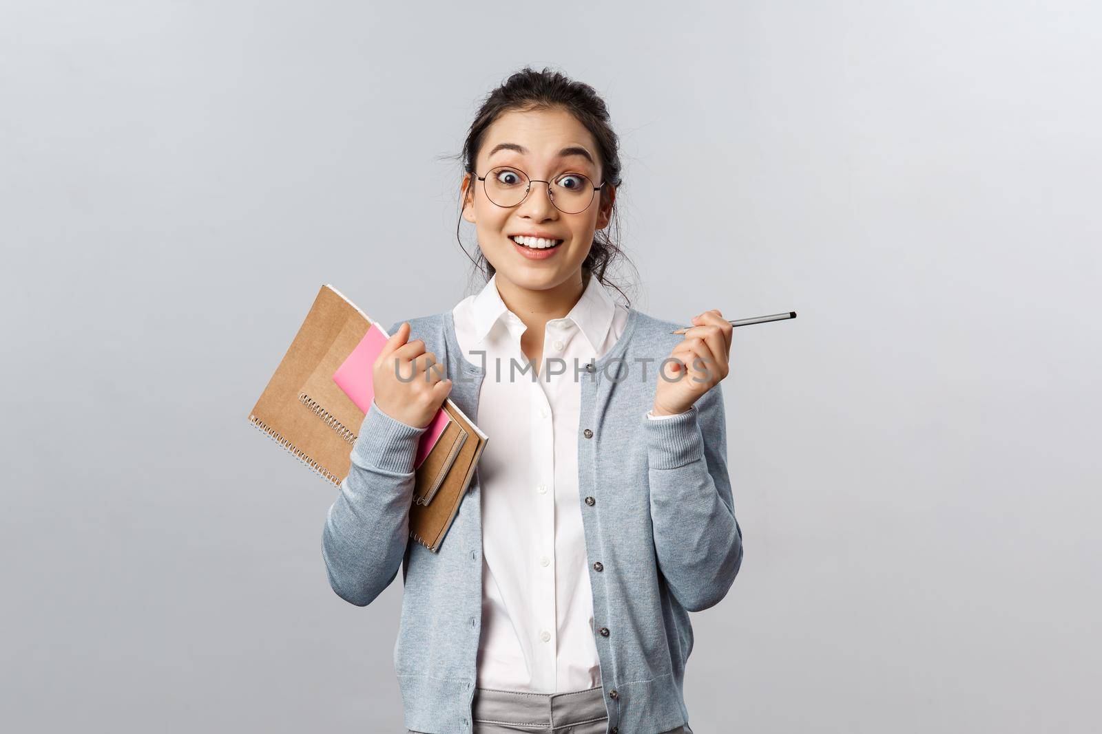 Education, teachers, university and schools concept. Enthusiastic, amused asian female in glasses, student gesturing with pencil in hands, holding notebooks, talking to classmate at campus hall by Benzoix