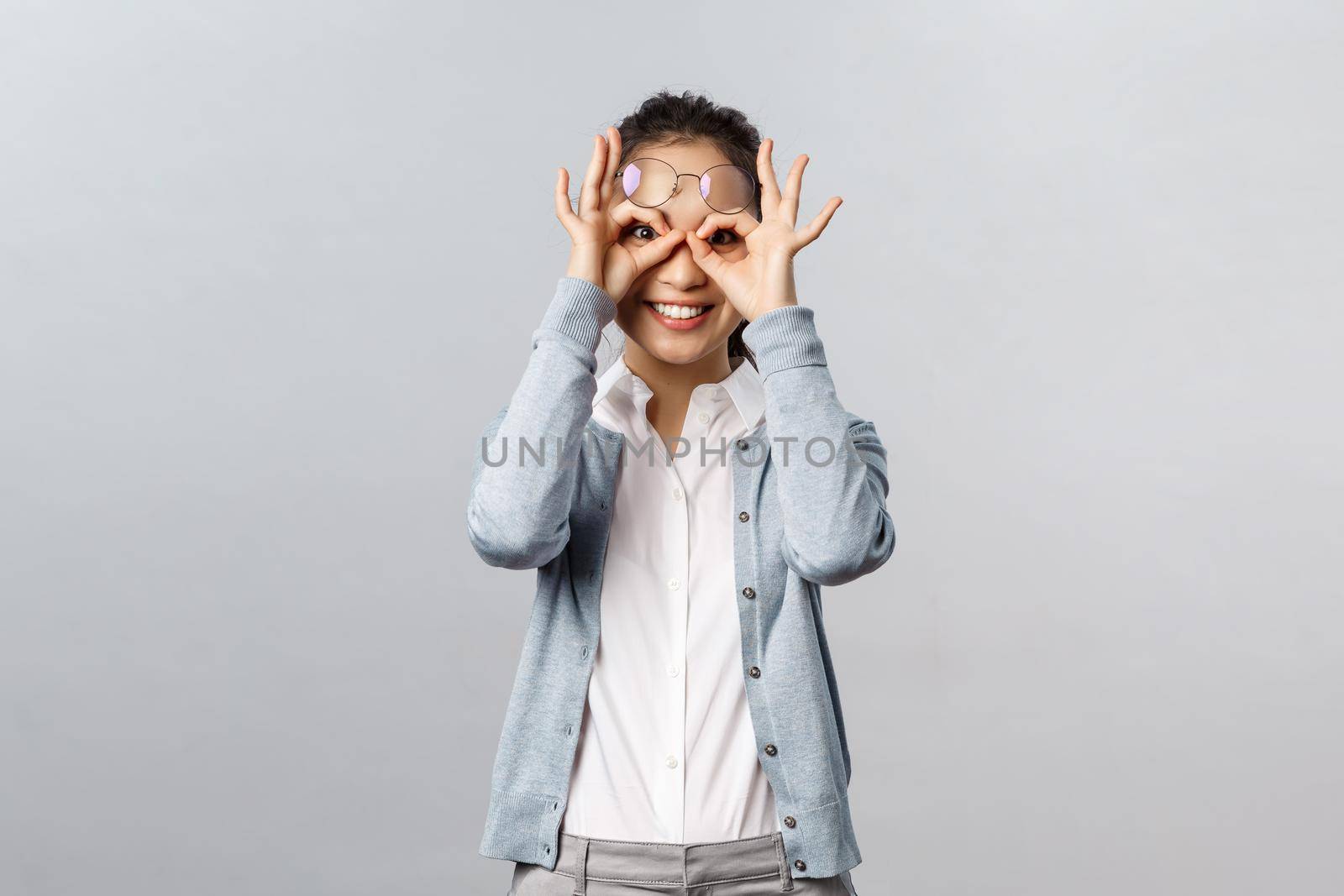 Lifestyle, people and emotions concept. Funny, enthusiastic asian nurse, nanny taking care of kids while parents working, showing funny expressions, make glass mask with fingers over eyes by Benzoix