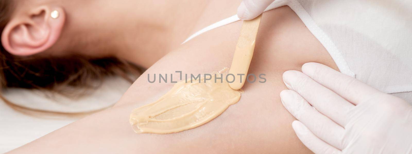 Depilation and epilation female armpit with liquid sugar paste by spatula. Hand of cosmetologist applying wax paste on armpit. Smooth underarm concept