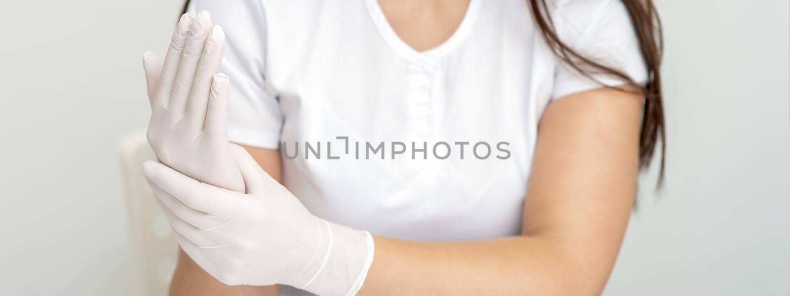Female hands putting on protective white latex medical gloves during epidemic in quarantine