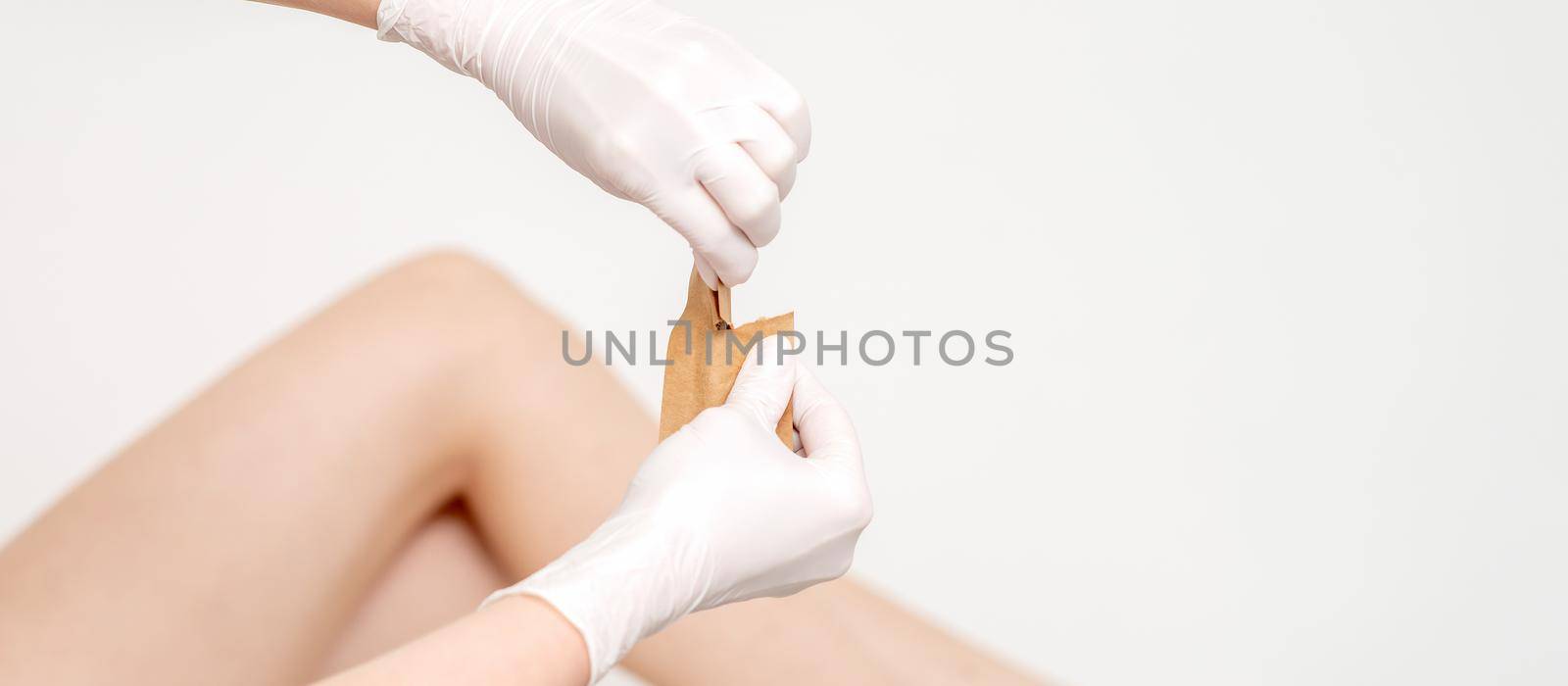 Human hands in protective gloves holding craft envelope with medical or beauty tools on background of female legs